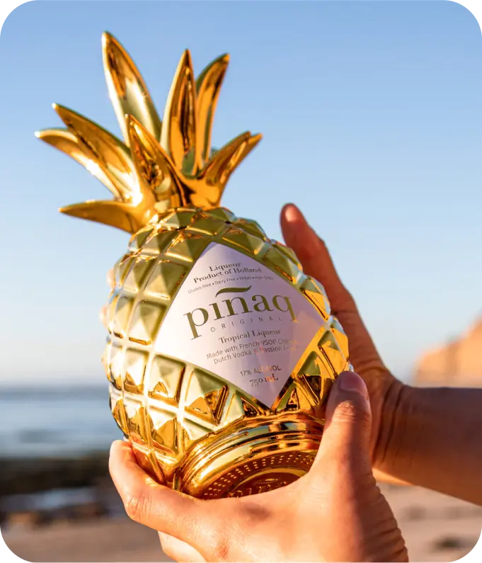 Jemand hält eine Flasche pinaq Original in den Händen, am Strand